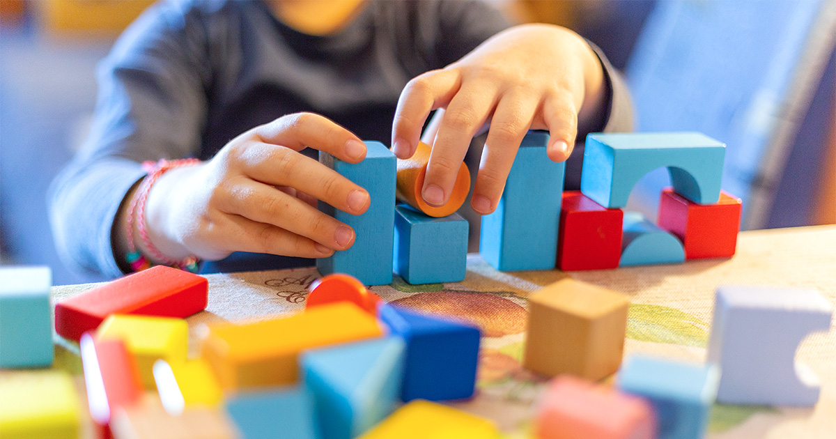 A child's hands stacking colorful wooden blocks on a table.