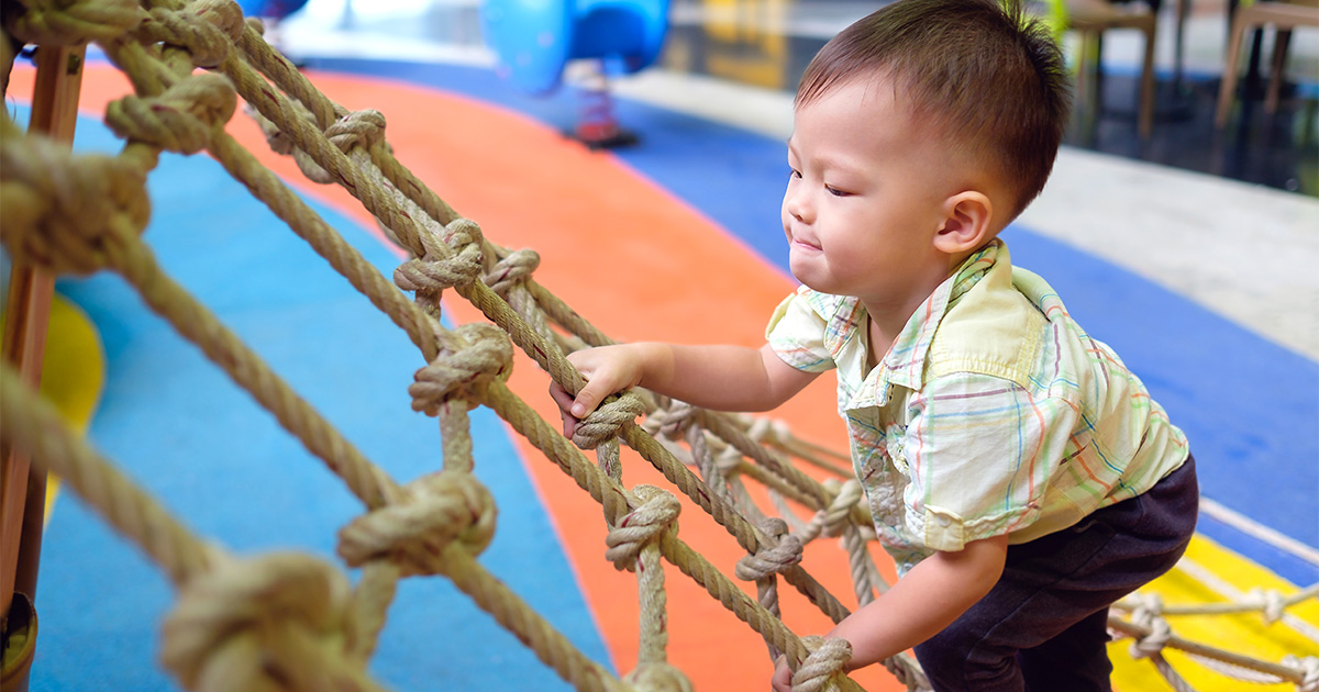Child climbing a rope net on a playground.